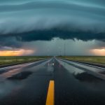 A highway through snowy prairie at dusk with storm clouds approaching, suggesting weather tracking for cross-border travel.