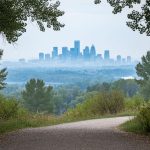 Calgary skyline partially obscured by light haze with trees in Fish Creek Park in the foreground, suggesting changing air quality conditions.