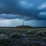 “Weather radar antenna on a hill overlooking a stormy Northern Alberta prairie with rain and dark clouds indicating moving precipitation.”